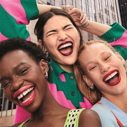3 mulheres maquilhadas a rir no meio de uma cidade