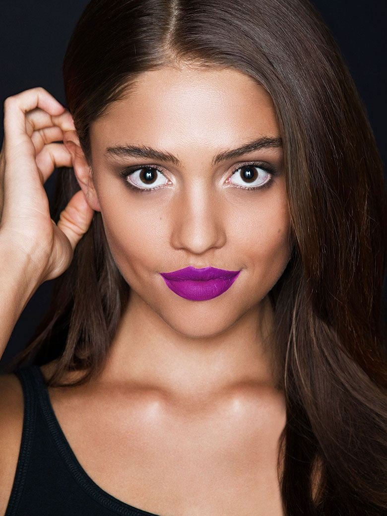 Mulher a utilizar o batom líquido mate de cor roxo da maybelline