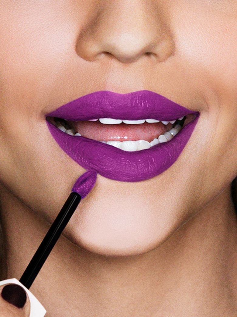 Mulher a aplicar batom em tom roxo da maybelline